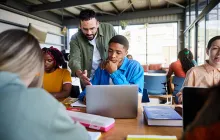 Trainer helping student on laptop in classroom