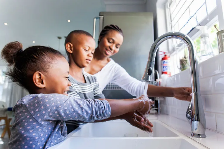 Mother and children washing hands at kitchen sink