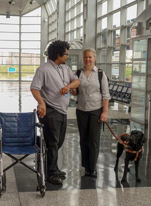 Image of a woman and her guide dog being assisted by an airport employee